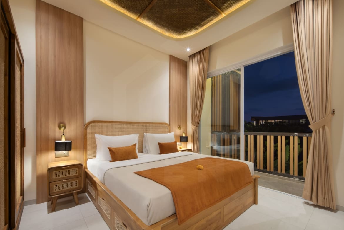 Elegant bedroom with warm wood accents, balcony access, and soft ambient lighting in a Bali villa