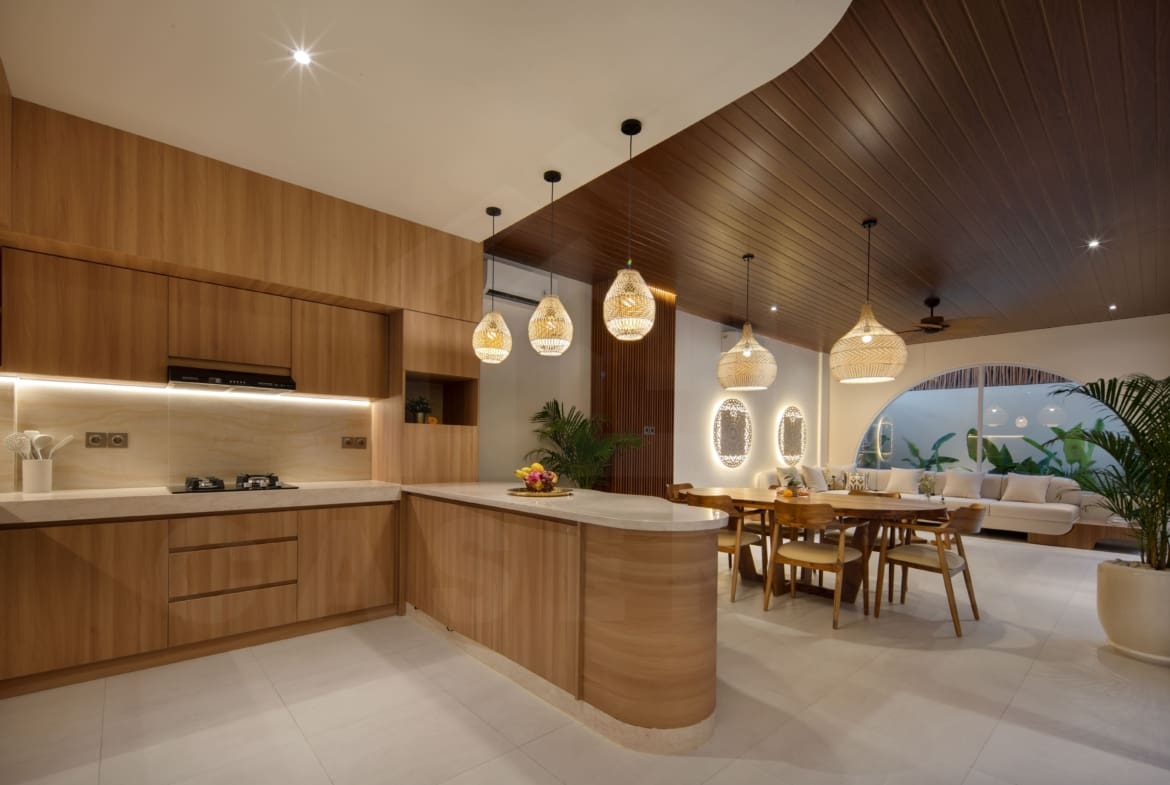 Warm open-plan kitchen, dining, and living area with wood finishes and pendant lighting in a modern Bali villa