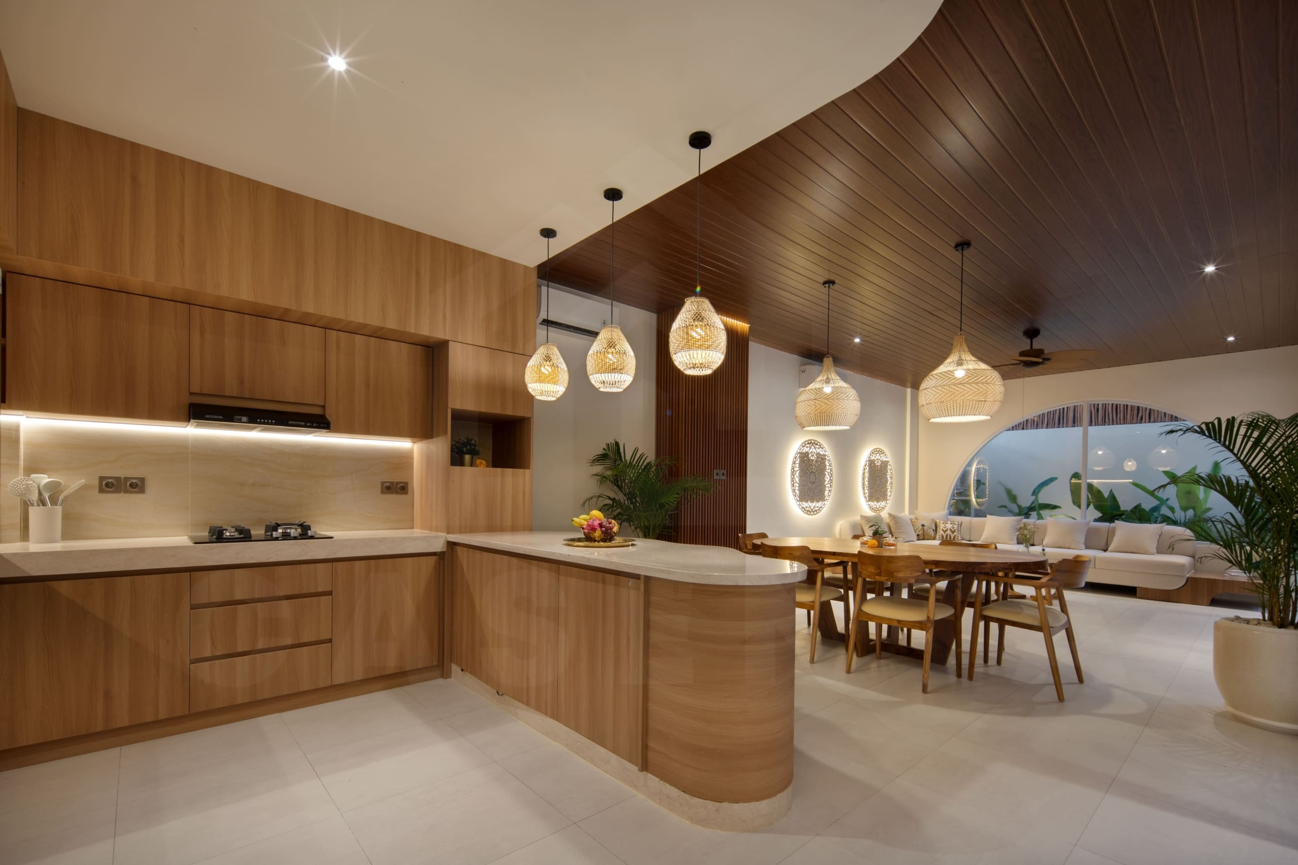 Warm open-plan kitchen, dining, and living area with wood finishes and pendant lighting in a modern Bali villa
