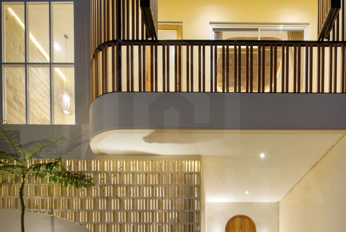 Modern villa facade with curved balcony, warm lighting, wood accents, and landscaped entrance in Bali