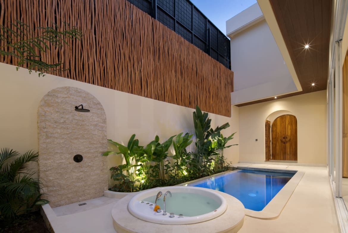 Private villa outdoor area with stone shower, jacuzzi, tropical plants, and wood accent wall