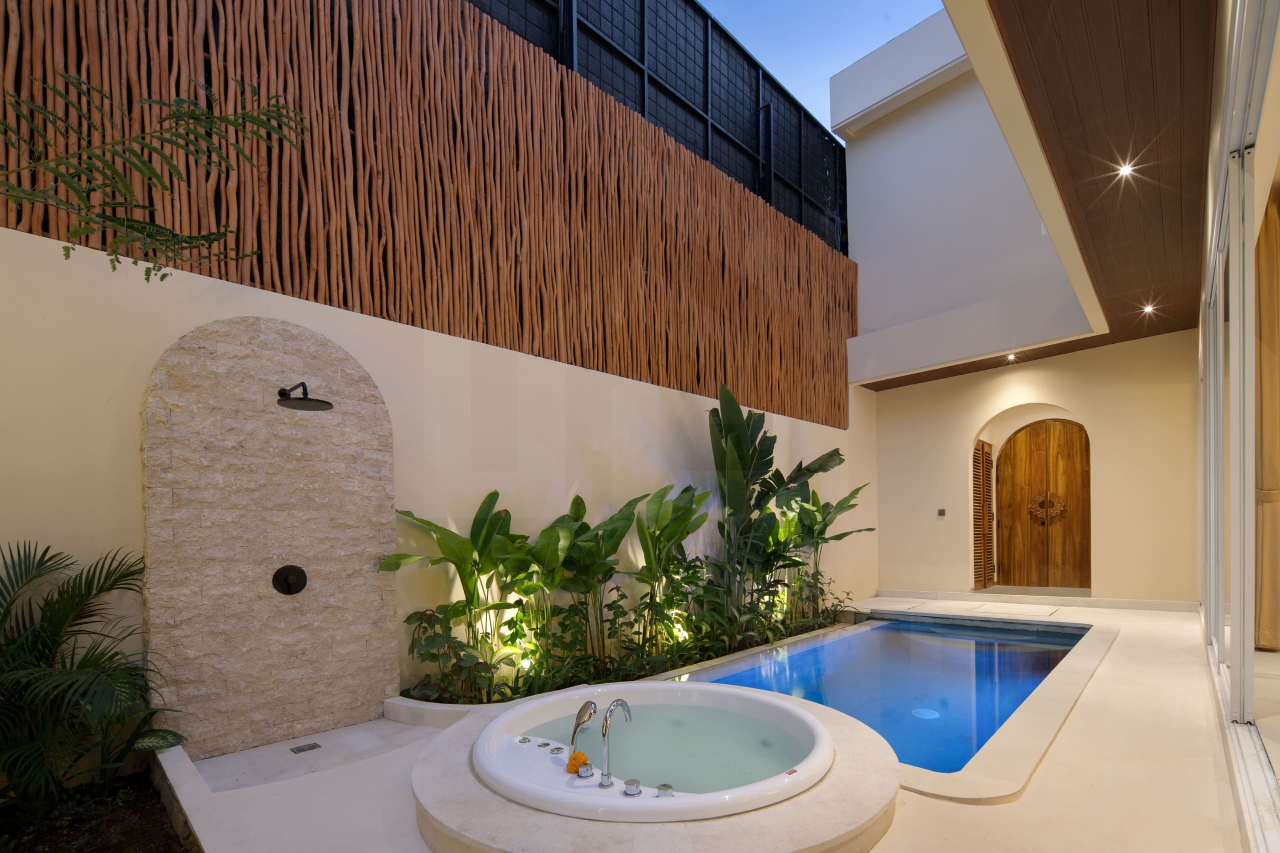Private villa outdoor area with stone shower, jacuzzi, tropical plants, and wood accent wall