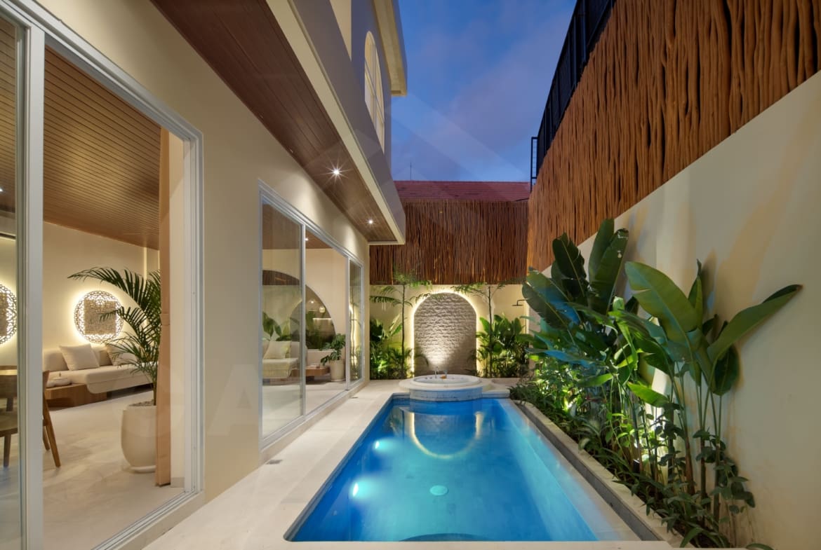 Private villa swimming pool with jacuzzi, tropical plants, and warm evening lighting