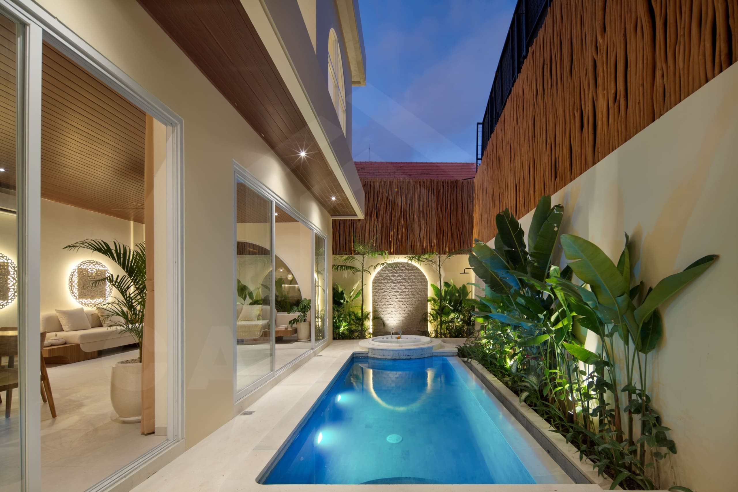 Private villa swimming pool with jacuzzi, tropical plants, and warm evening lighting