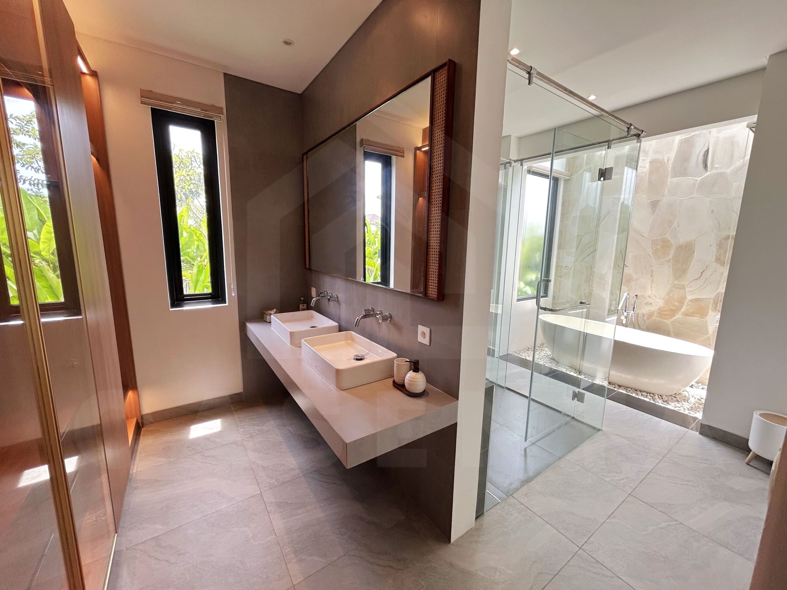 Elegant villa bathroom with double vanity, glass shower, and stone-wall bathtub area