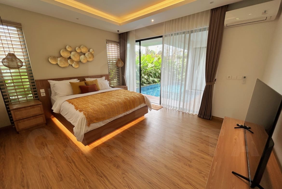Spacious villa bedroom with warm lighting, pool access, and floor-to-ceiling windows