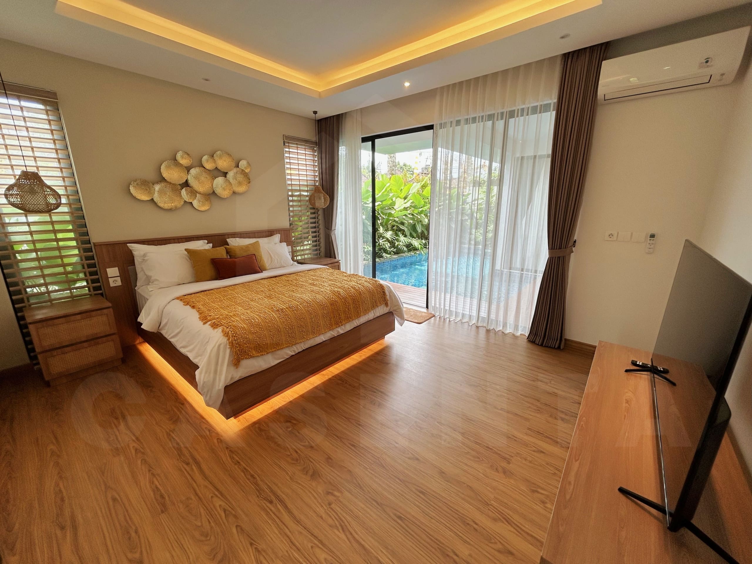 Spacious villa bedroom with warm lighting, pool access, and floor-to-ceiling windows