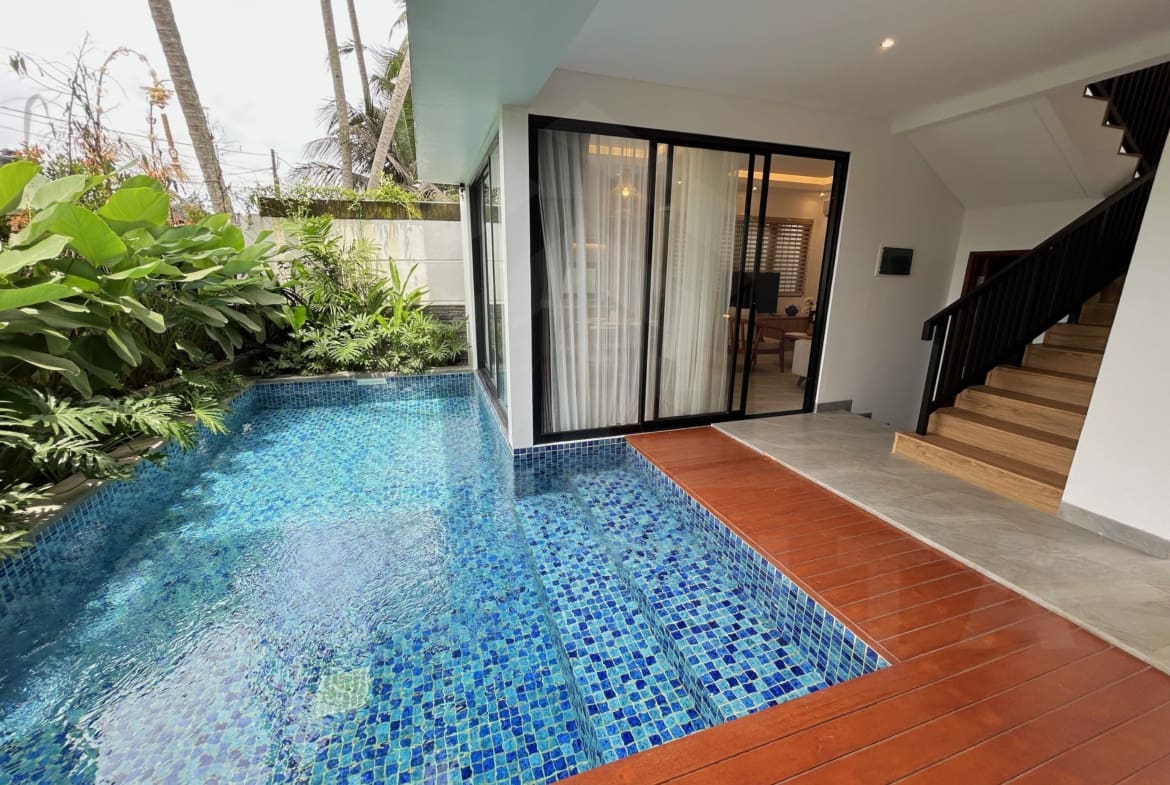 Compact villa pool with blue mosaic tiles beside bedroom sliding glass doors and lush plants.