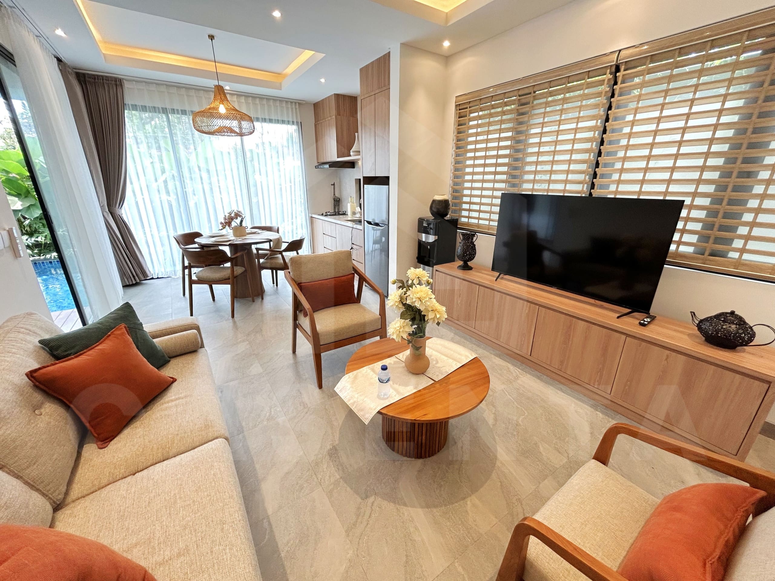 Bright living and dining area with wood furniture, large windows, and poolside views.