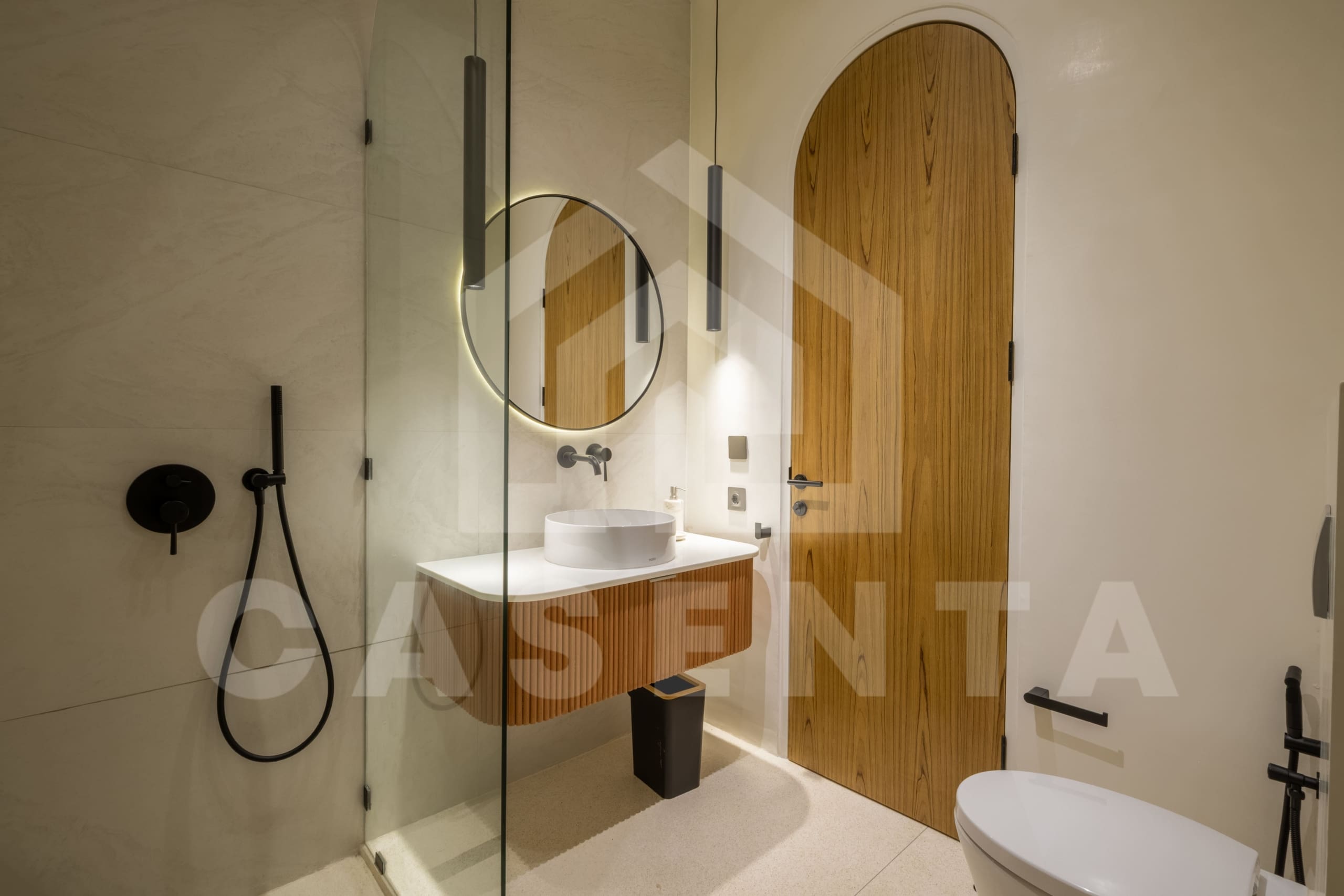Contemporary bathroom with arched wooden door and illuminated circular mirror