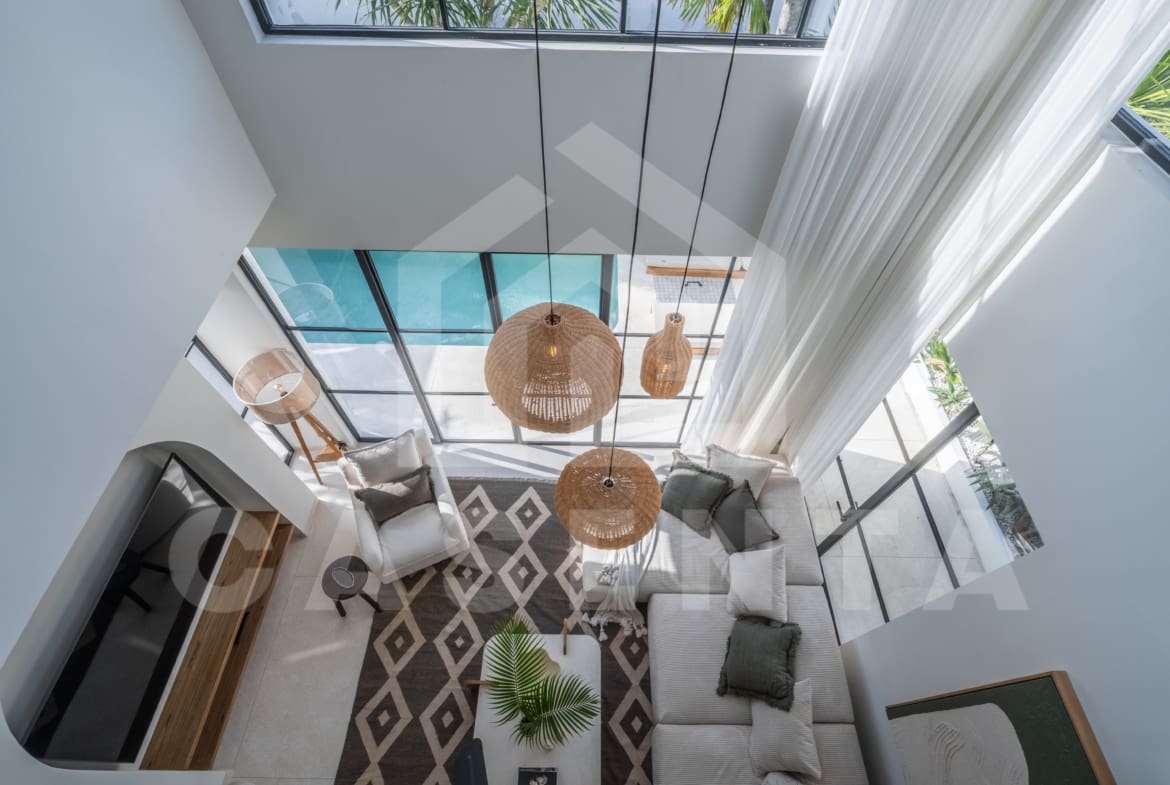 Double-height living room overlooking the pool with rattan pendant lights