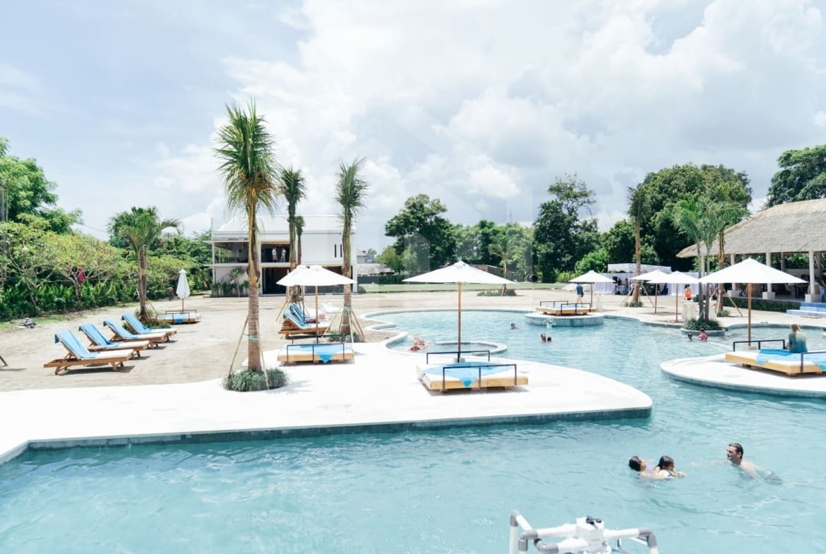 Lagoon-style public pool at Jimbaran villa with sunbeds, palm trees, and island daybeds
