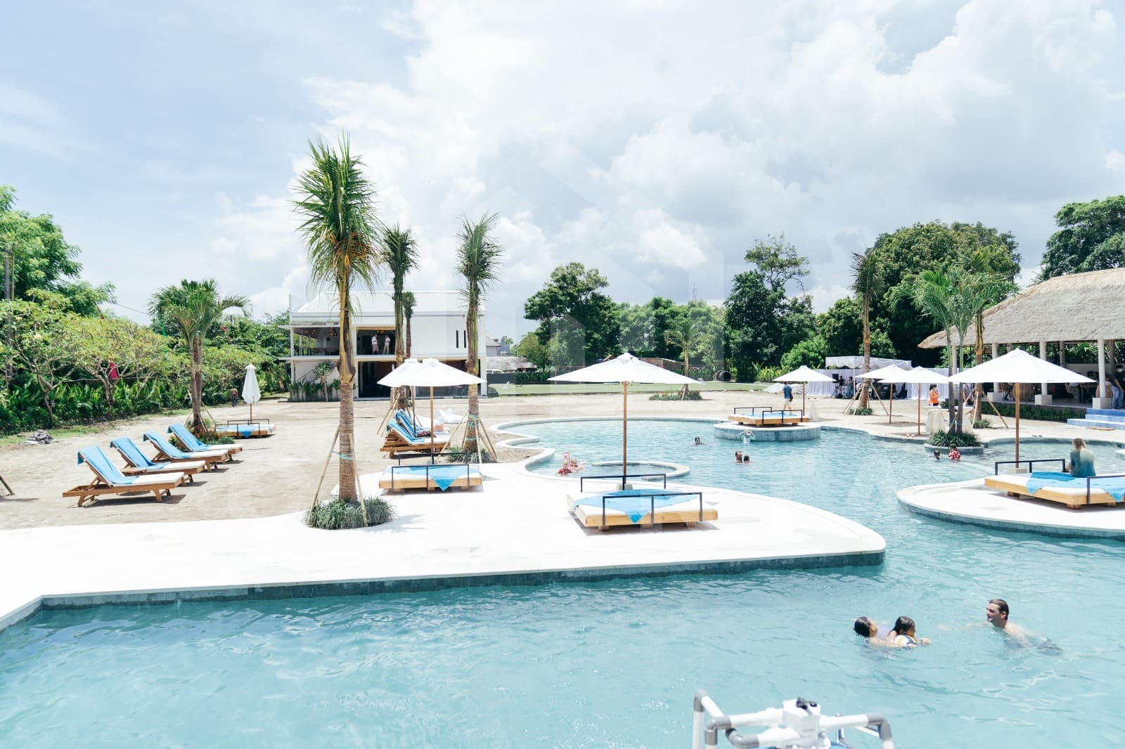 Lagoon-style public pool at Jimbaran villa with sunbeds, palm trees, and island daybeds